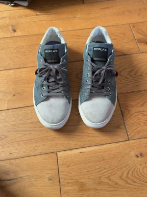 Gråa Replay sneakers i mocka och textil - Snygga sneakers från Replay i grå mocka och textil med vita sulor och mörkgrå skosnören. Storlek 42 Klassisk låg modell med Replay-logga på plösen. Hör av er vid funderingar.