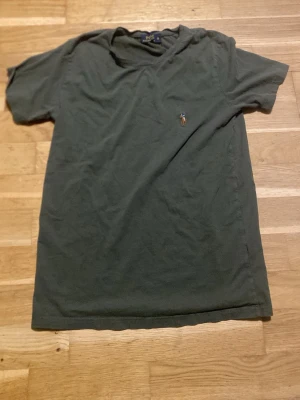 Mörkgrön t-shirt från Polo Ralph Lauren - En mörkgrön t-shirt från Polo Ralph Lauren med klassisk passform och korta ärmar. T-shirten har en liten broderad logga på bröstet och är tillverkad i mjuk bomull. Perfekt till jeans eller shorts för en enkel och stilren look.