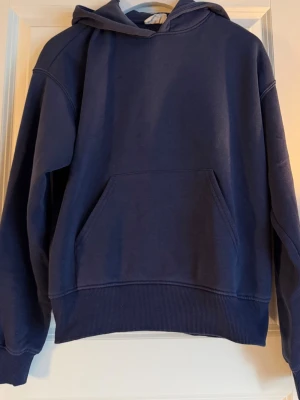 Mörkblå hoodie från Gina Tricot - Mörkblå hoodie från Gina Tricot, basically basics-kollektionen. Klassisk modell med huva och stor magficka framtill. Tillverkad i mjukt bomullsmaterial och har ribbade muddar vid ärmslut och nederkant. Perfekt för en chill och avslappnad stil.