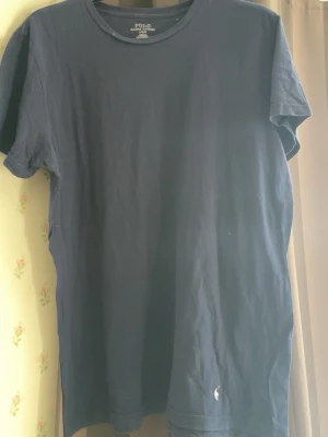 Mörkblå t-shirt från Polo Ralph Lauren - Klassisk mörkblå t-shirt från Polo Ralph Lauren med den ikoniska vita loggan broderad längst ner. T-shirten har rund halsringning och korta ärmar. Tillverkad i mjuk bomull för en skön känsla.