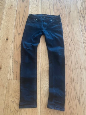 Nudie Jeans Slim Fit W29 L32 Mörkblå Premium Denim - Snygga mörkblå slim fit jeans med klassisk femficksdesign och raka ben. Jeansen har en stilren look och passar perfekt till en avslappnad streetstyle. Materialet känns mjukt och följsamt, vilket gör dem bekväma att bära hela dagen. W29 L32