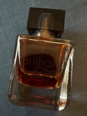 Brilliant Look Eau de Parfum - Brilliant Look Eau de Parfum från LR har en elegant glasflaska med mörk bärnstensfärgad vätska och svart fyrkantigt lock. Doften är blommig och kryddig med noter av bergamott, päron, fresia, jasmin, apelsinblomma, patchouli, vanilj och kola.