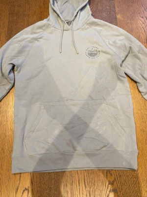 Ljusgrå hoodie med tryck - Ljusgrå hoodien som är köpt i Nya Zeeland för 1099 kr, har användts max 2 gånger så är i ny skick. Hör av dig vid fler frågor!