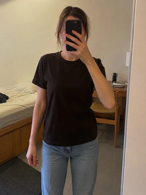 H&M Basic brun T-shirt XS – minimalistisk - Enkel mörkbrun T-shirt från H&M Basic i storlek XS. Klassisk modell med rund hals och kort ärm. Snygg neutral chokladbrun färg som är lätt att matcha med jeans.  Fint begagnat skick. Se bilder för passform och skick.