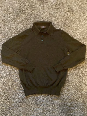 Mörkgrön merinopiké - Mörkgrön stickad pikétröja med lång ärm och klassisk krage ifrån Ströms. Gjord av 100% ”pura lana vergine pure new merino extrafine” Kommer med en extra knapp. Tröjan har tre knappar framtill och ribbade muddar vid ärmslut och nederkant. Perfekt för dig som gillar en stilren och enkel look. Nypris ligger på 1799kr. Skicka dm gärna om du har frågor eller vill ha någon extra bild m.m