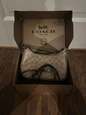 Coach Teri shoulder bag in beige signature canvas - Snygg beige handväska från Coach med det klassiska monogrammönstret och silverfärgade detaljer. Väskan har justerbar axelrem och dragkedja upptill. Perfekt för dig som vill ha en stilren och trendig accessoar till din outfit.