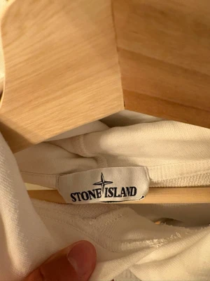 Vit hoodie från Stone Island - Säljer en stilren vit hoodie från Stone Island med klassisk huva och långa ärmar. Hoodien har ribbade muddar och är tillverkad i mjukt material som känns skönt mot huden. Perfekt för dig som gillar minimalistisk och clean streetwear.