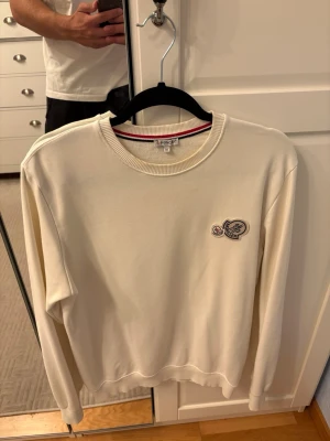 Vit sweatshirt från Moncler - Snygg vit sweatshirt från Moncler med rund halsringning och ribbade muddar. Tröjan har två broderade Moncler-loggor på bröstet och en clean, minimalistisk look. Perfekt för dig som gillar stilrena plagg med exklusiv känsla. Små fläckar vid halsen av parfym 