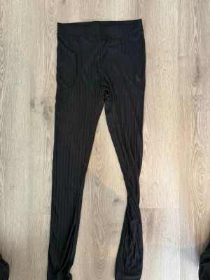 Svarta leggings med diskreta ränder - Säljer ett par svarta leggings med diskreta vertikala ränder och bred resår i midjan. De har två fickor framtill och är tillverkade i ett stretchigt material som sitter skönt på kroppen. Perfekta för en avslappnad och trendig look.