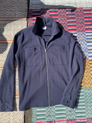 Mörkblå overshirt från Selected Homme - Säljer en stilren mörkblå overshirt från Selected Homme med två bröstfickor och dragkedja framtill. Overshirten har lång ärm med knapp vid ärmslut och är gjord i ett mjukt material som känns bekvämt. Perfekt att slänga på över en t-shirt.