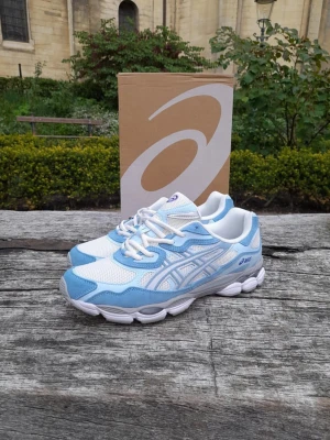 Oandvända Asics vita och ljusblå sneakers - Säljer ett par fräscha Asics sneakers i vitt och ljusblått. Skorna har mesh- och syntetpaneler för bra andningsförmåga och komfort. Klassisk Asics-logga på sidan och en chunky vit sula som ger en sportig vibe. Perfekta för dig som gillar stilrena och bekväma sneakers.