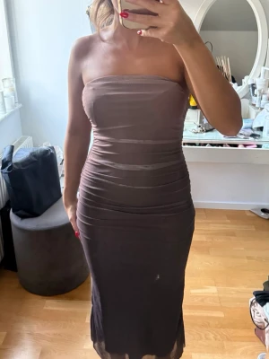 Brun axelbandslös långklänning - Säljer en brun axelbandslös långklänning med tight passform. Klänningen har en enkel, stilren design och är gjord i ett stretchigt material som formar sig efter kroppen. Perfekt för dig som gillar minimalistisk och elegant stil.
