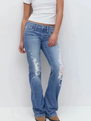 Blå slitna bootcut jeans - Säljer ett par ljusblå bootcut jeans med slitningar.  Kostar 430 i orginal pris och är som helt nytt skick, har använt dom cirka 2 gånger. Jeansen har klassisk femficksmodell och låg midja. Perfekta för en avslappnad och trendig look.