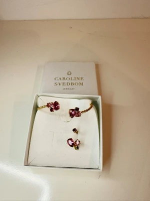 Guldarmband med rosa stenar - Snyggt armband från Caroline Svedbom i guldton med stora rosa kristaller. Armbandet har en öppen design och dekoreras med glittrande stenar i olika nyanser av rosa. Perfekt för att ge din outfit extra bling. Även ett paket här med, med den rosa fina ringen och den fantastiska modellen på ringen !! Helt underbara, älskar färgen, men har redan lite mkt hehe, säljer samma här gärna helst i ett paket( par ) men skulle man önska nått annat hör av er ! Jätte fint skick, knappt använt ! ✨
