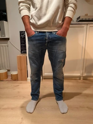 Dondup George  - Säljer ett par blå jeans med snygga slitningar och en relaxed fit. Jeansen har klassisk femficksdesign och knappgylf. Perfekta för dig som gillar en avslappnad och trendig stil.