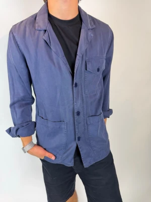 Blå overshirt från A days march  - Stilren blå overshirt med tre framfickor och knäppning framtill. Skjortkrage och långa ärmar som kan vikas upp för en avslappnad look. Tillverkad i ett mjukt, vävt material som ger en casual vibe. Från a days march 