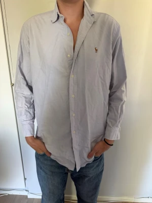 Ljusblå Ralph Lauren skjorta  - Klassisk ljusblå skjorta med knappar framtill och en liten broderad logga på bröstet. Skjortan har lång ärm, normal passform och en mjuk krage. Perfekt till jeans eller chinos för en clean och stilren look. Ralph Lauren loggan är brun. Har knappt använt den. Hör av dig om du har några frågor eller vill ha fler bilder! Pris kan diskuteras. 