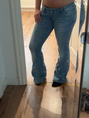 Ljusblå bootcut jeans - Säljer ett par ljusblå bootcut jeans med klassisk femficksdesign och låg midja. Jeansen har en snygg tvättad look och är tillverkade i denim med lite stretch för extra komfort. Perfekta för dig som gillar en avslappnad men trendig stil.