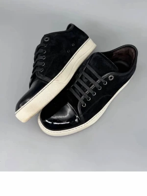 Lanvins - Stilrena svarta sneakers med vit sula och snygga lackdetaljer på tån. Ovandelen är i mocka och skon har svarta skosnören samt metallfärgade öljetter. Perfekta för dig som gillar en clean och modern look.