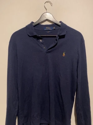 Mörkblå långärmad henley tröja från Polo Ralph Lauren - Säljer en mörkblå långärmad tröja från Polo Ralph Lauren med klassisk krage och broderad logga på bröstet. Tröjan har knappar vid halsen och är tillverkad i mjuk bomull. Perfekt för en stilren och avslappnad look. Priset är inte hugget i sten, släng iväg ett dm om du har några frågor 😁
