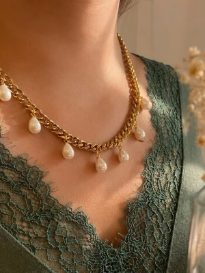 Guldhalsband med droppformade pärlor - Snyggt halsband i guldfärgad rostfritt med droppformade vita pärlor som hänger längs kedjan. Kedjan är lite chunky och ger en cool kontrast till de eleganta pärlorna. Perfekt för att lyfta vilken outfit som helst med en trendig touch.