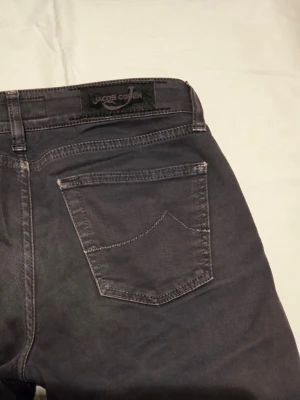 Jeans från Jacob Cohen - Snygga svartgråa jeans från Jacob Cohen i storlek W27. Klassisk femficksmodell. Jeansen har diskreta sömmar och en svart patch med logga bak i midjan. Perfekta för dig som gillar stilrena och tidlösa plagg.