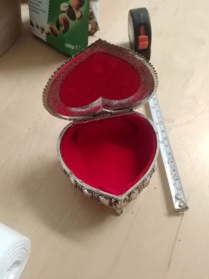 Hjärformad smyckesask i metall - Unik hjärtformad smyckesask i silverfärgad metall med detaljerade mönster och rödfärgad sammetsinredning. Perfekt för att förvara småsaker eller smycken. Asken står på små dekorativa fötter och har ett elegant lock.