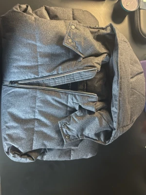 Grå dunväst med huva - Snygg mörkgrå dunväst med avtagbar huva och två dragkedjeförsedda fickor framtill. Västen har en rak passform och quiltad design med breda paneler. Perfekt för lager-på-lager och håller dig varm under kyliga dagar.