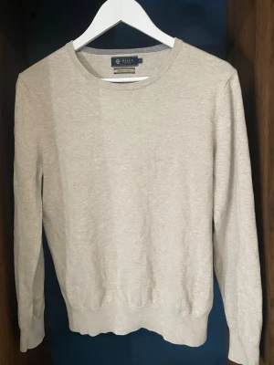Beige Riley tröja  - Snygg beige tröja från Riley i premium bomull. Tröjan har rund halsringning, långa ärmar och ribbade muddar vid ärmslut och nederkant. Enkel och stilren design som passar till det mesta.