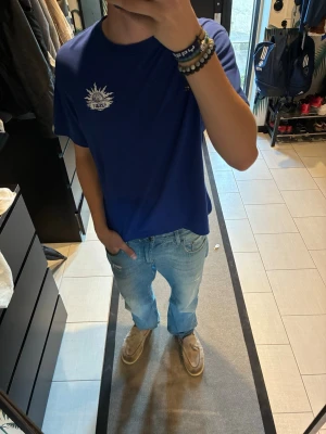 REPLAY - Snygg blå t-shirt med vitt tryck på bröstet och stort tryck på ryggen. T-shirten har en klassisk passform 