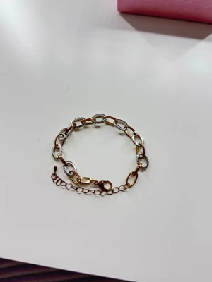 Länkarmband i guld och silverfärg - Snyggt armband med ovala länkar i både guld- och silverfärg. Armbandet har en justerbar kedja och karbinlås. Länkarna är delvis dekorerade med små glittrande detaljer som ger en cool kontrast. Perfekt accessoar för att lyfta din stil.