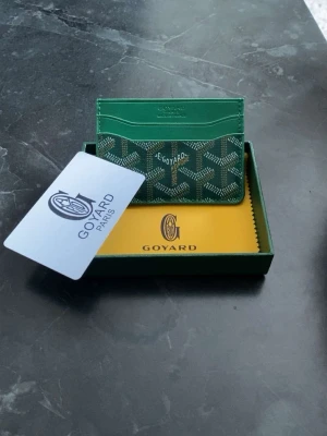 GY plånbok - Snygg grön plånbok från GY med klassiskt mönster och guldfärgad logga. Tillverkad i läder och canvas