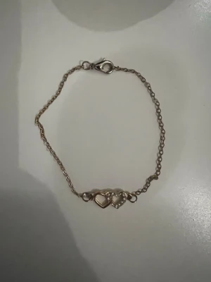 Guldigt armband med hjärthängen💛 - Snyggt och tunt armband i guldfärgad metall med två hjärtformade hängen, varav ett är dekorerat med små glittrande stenar. Kan användas för både vuxna och barn! 