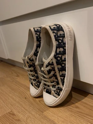 Dior Oblique låga sneakers - Snygga låga sneakers från Dior med klassiskt blått och beige Oblique-mönster. Skorna har vita sulor med 'Christian Dior' tryckt på sidan och vita snören. Ovandelen är i textil och sulan i gummi. Perfekta för dig som vill ha en trendig och exklusiv look. (Hjälper min kompis att sälja dessa då dom inte kommer till användning längre) 