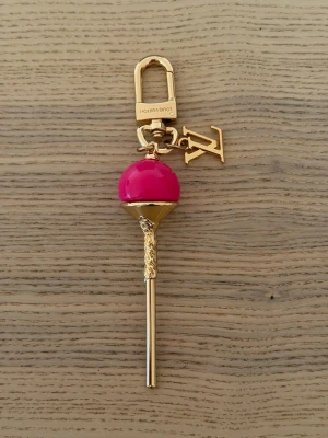 Vuitton nyckelring klubba guldrosa - Unik nyckelring från  Vuitton i form av en klubba. Färgerna är guld och starkt rosa, med LV-logga som hänge. Tillverkad i metall med glansig finish och detaljerad design. Perfekt accessoar för att piffa upp väskan eller nyckelknippan.