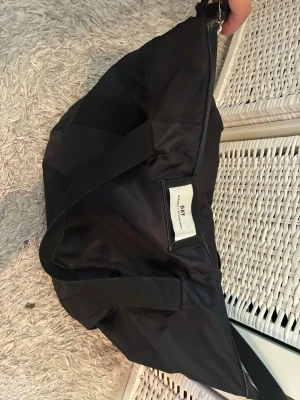 Svart shoppingväska från DAY - Stor svart shoppingväska från DAY Birger et Mikkelsen i slitstarkt nylonmaterial. Väskan har breda handtag och en praktisk dragkedja upptill. Perfekt för att bära med sig allt man behöver under dagen. Klassisk och enkel design med logga på framsidan.