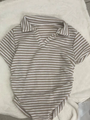 Beige och vit randig t-shirt med krage - Säljer en snygg t-shirt med korta ärmar och krage i beige och vitt randigt mönster. 