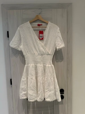 Vit kort klänning med broderie  - Perfekt för sommarens alla fester, midsommar eller student! Otroligt söt vit klänning i 100% bomull med vackra hålbroderier. Märke: RYVLS ( kids brand store) Storlek: 170/176 (passar XS/S då midjan har stretchig smock) Detaljer: Romantisk omlottringning, foder i bomull och jättefin passform. Skick: Helt ny! Prislapp kvar (699 kr). 🏠Kommer från ett rök- och djurfritt hem. Fraktar samma dag! Säg till om du har frågors💞 