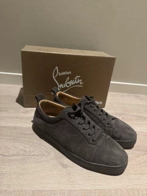 Gråa sneakers från Christian Louboutin - Stilrena gråa sneakers från Christian Louboutin i mocka med matchande grå snörning och sula. Låg modell med klassisk siluett och diskreta detaljer. Insidan är fodrad i beige läder för extra komfort. Storlek 43. Några stygn har gått bort.
