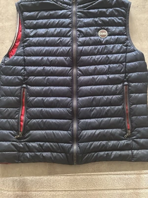 Mörkblå quiltad dunväst från Colmar - Snygg mörkblå dunväst från Colmar med quiltad design och röda detaljer på insidan. Pris är inte hugget i sten