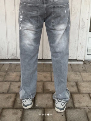 Grå raka jeans med färgstänk - Grå jeans i rak modell med stora bakfickor och tydliga vita färgstänk för en cool och avslappnad vibe. Jeansen är gjorda i klassisk denim och har en vintagekänsla som passar perfekt till streetwear och trendiga outfits.