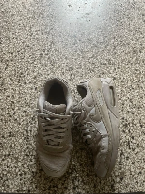 Vita Nike Air Max sneakers - Säljer ett par klassiska vita Nike Air Max sneakers med mesh och läderdetaljer. Skorna har en chunky sula med synlig Air-enhet och Nike-logga på sidan. Perfekta för dig som gillar sportig och stilren look.
