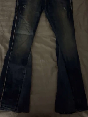 Mörkblå bootcut jeans med slitningar - Snygga mörkblå bootcut jeans med ljusa slitningar och markerade sömmar längs benen. Jeansen har en klassisk femficksmodell och är tillverkade i denim. Perfekta för en avslappnad och trendig look.