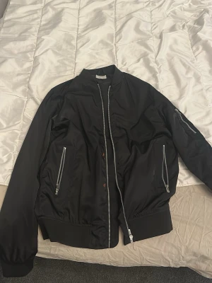 Svart bomberjacka med dragkedjor - Svart bomber jacka från jack and jones. Lite röd färg på framsidan 