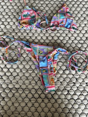 Färgglad bikini med tropiskt mönster - Säljer en bikini med tropiska motiv som palmer, apelsiner och strandbilder i olika färger som rosa, blå, lila och grön. Både överdel och underdel har knytband på sidorna och över axlarna. Perfekt för sommarens strandhäng! Helt nytt skick! en del = 65 kr, 2 delar = 110 kr