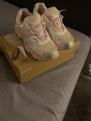 Asics sneakers i rosa och vitt - Snygga Asics sneakers i en fräsch kombination av ljusrosa, vitt och silver. Skorna har klassisk låg profil, meshpaneler för andningsförmåga och detaljer i syntetmaterial. Perfekta för dig som gillar sportig stil med en touch av pastell.