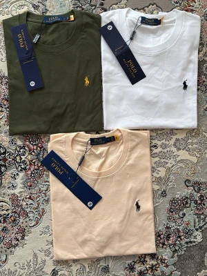 3-pack t-shirts från Polo Ralph Lauren - Säljer ett 3-pack t-shirts från Polo Ralph Lauren i färgerna olivgrön, vit och beige. Alla har klassisk passform, rund halsringning och den ikoniska broderade loggan på bröstet. Tillverkade i mjuk bomull för maximal komfort.