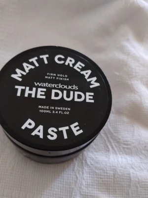 Waterclouds The Dude Matt Cream Paste - Matt Cream Paste från Waterclouds The Dude är en hårstylingprodukt med fast stadga och matt finish. Burken är svart med vit text och innehåller 100 ml. Perfekt för dig som vill ha en naturlig look utan glans. Oöppnad.