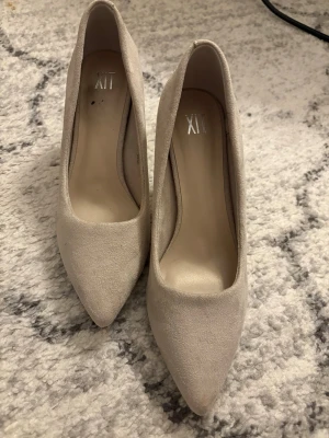 Beige spetsiga pumps i mockaimitation - Snygga pumps i beige mockaimitation med spetsig tå och smal klack. Klassisk och stilren design som passar till många olika looks. Skorna har en låg till medelhög klack och är helfärgade utan dekorationer. Aldrig använda. 