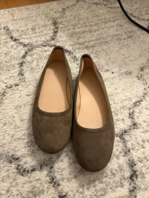 Bruna ballerinaskor i mockaimitation - Snygga ballerinaskor i en mjuk brun mockaimitation med rund tå och klassisk design. Skorna har en enkel och stilren look som passar till många outfits. Fodret är ljust och sulan är platt för en bekväm känsla hela dagen. Använda endast 1 gång. 